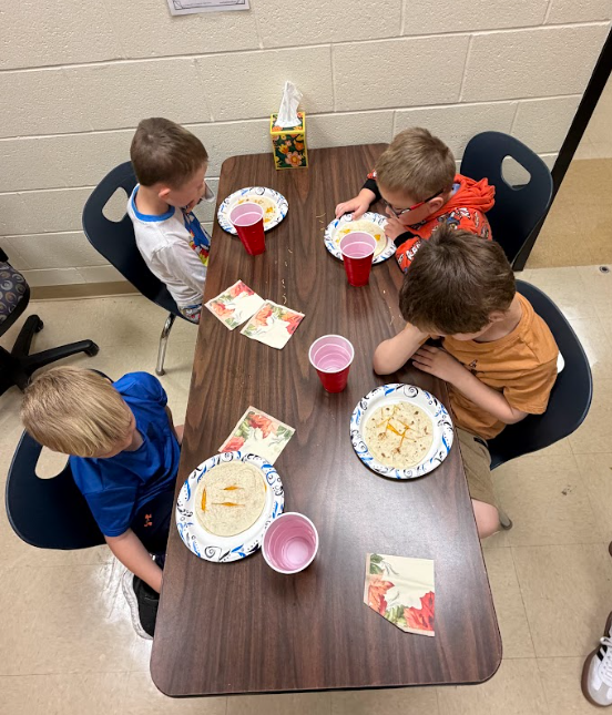 Five students sitting at a table with pumpkin plates in front of them eating quesadillas