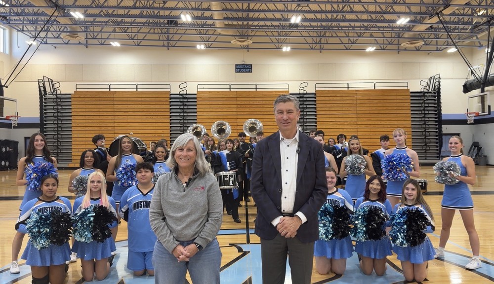 Superintendent and board president standing infront of the Mountain Range band, cheer and poms teams