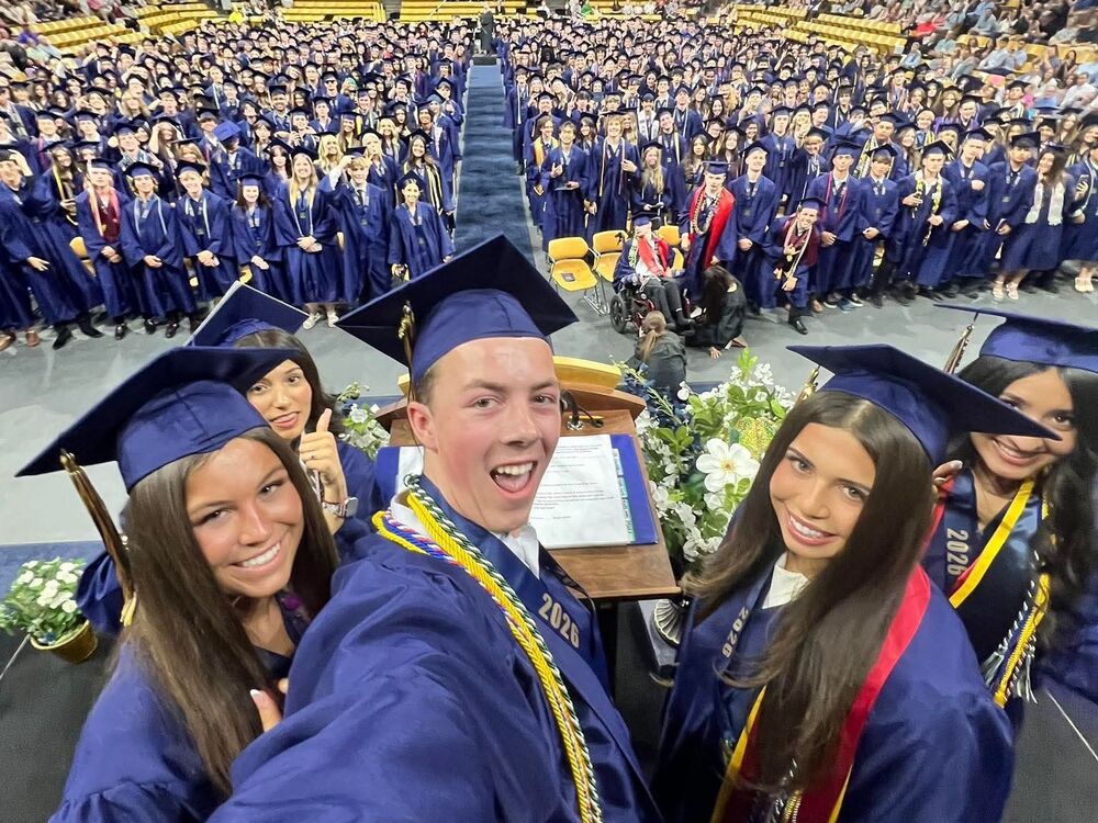 Graduates taking a selfie with the entire class in the back