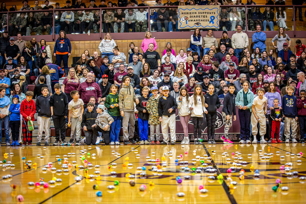 Students throwing rubber stars onto a gym floor in front of a packed crowd