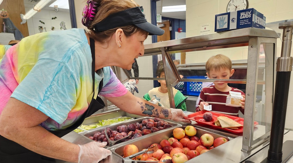 Lunch lady serving an apple to two elementary students