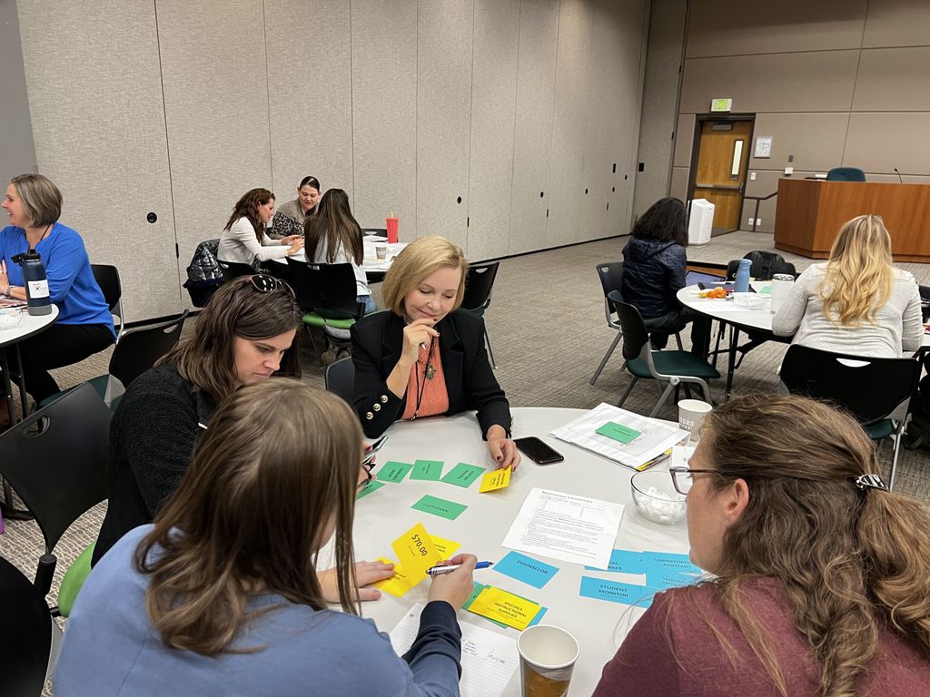 Parents looking at different colored cards that indicate different costs as they try to put together a mock school budget.