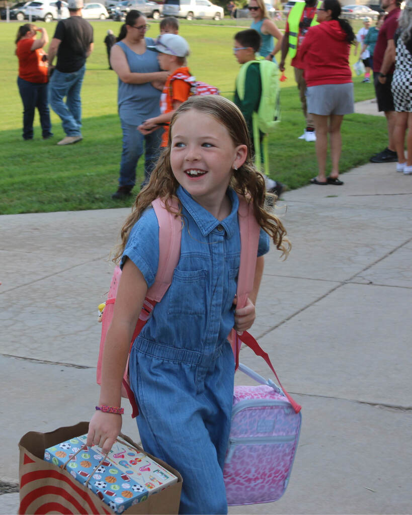 Student smiling walking into school carrying her supplies