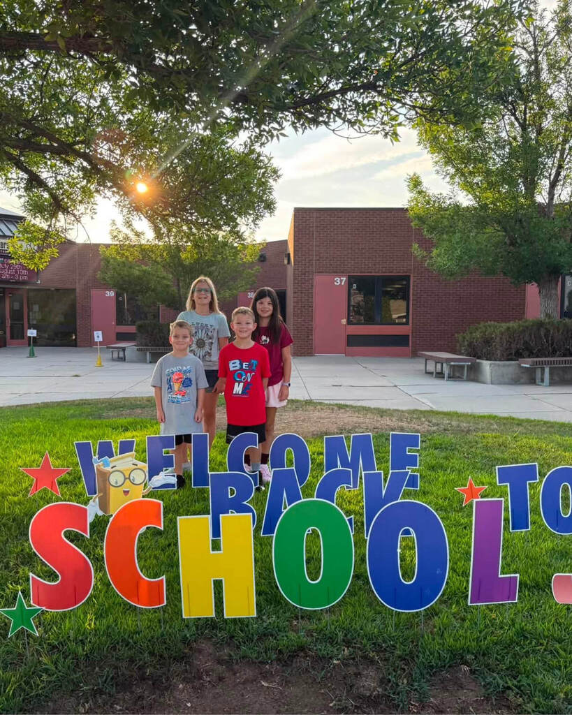 Students posing with a Welcome Back to School yard sign in front of school