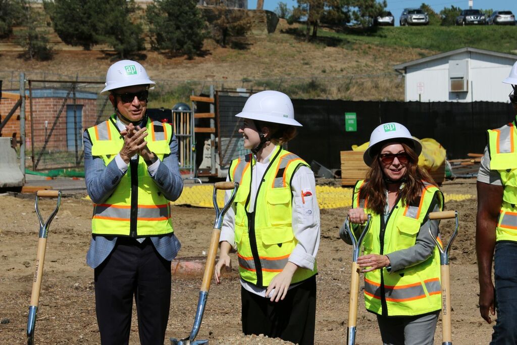 Three people in hard hats and vests with shovels celebrating