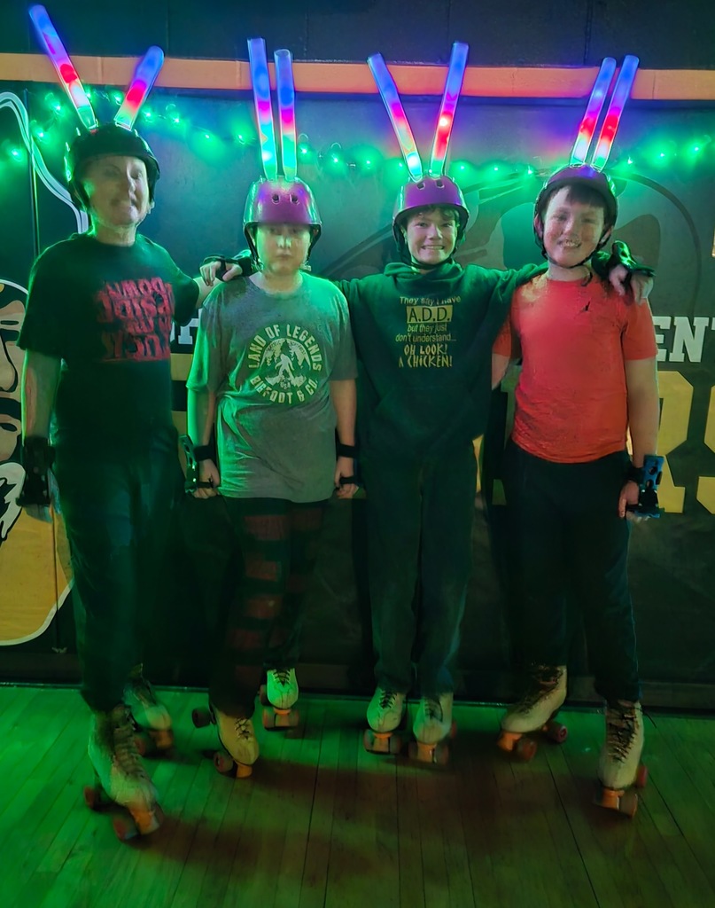 four male students, upper elementary students in skates under glow lights with light up sticks for glow skating