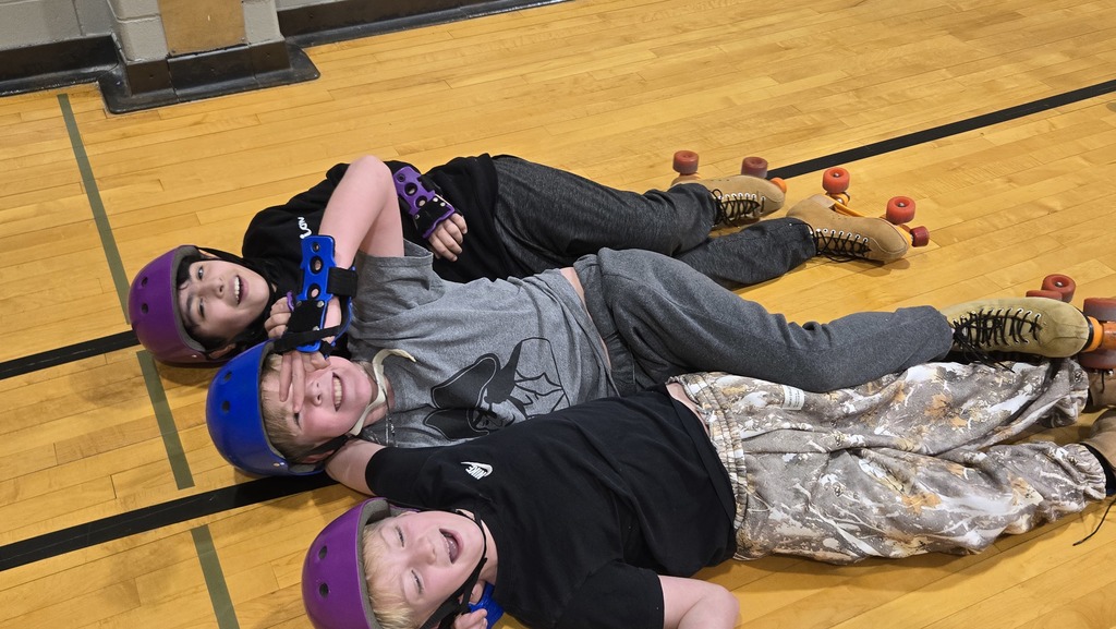 three students in skates and helmets laying on the gym floor smiling