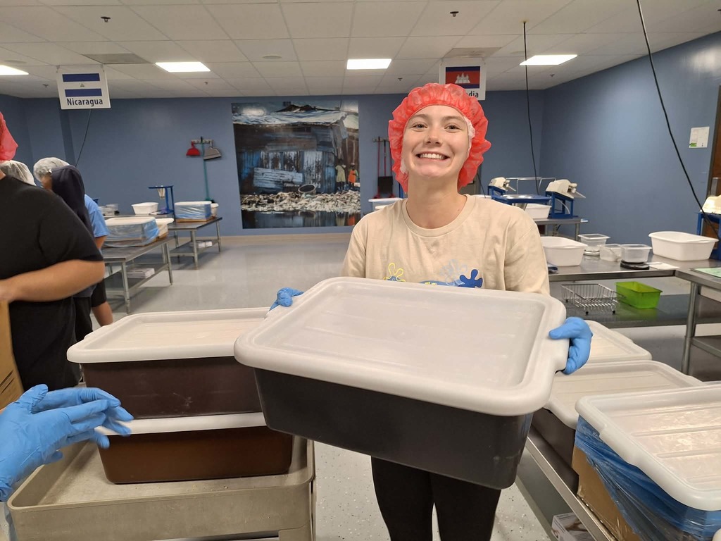 student holding bin wearing hair net and smiling