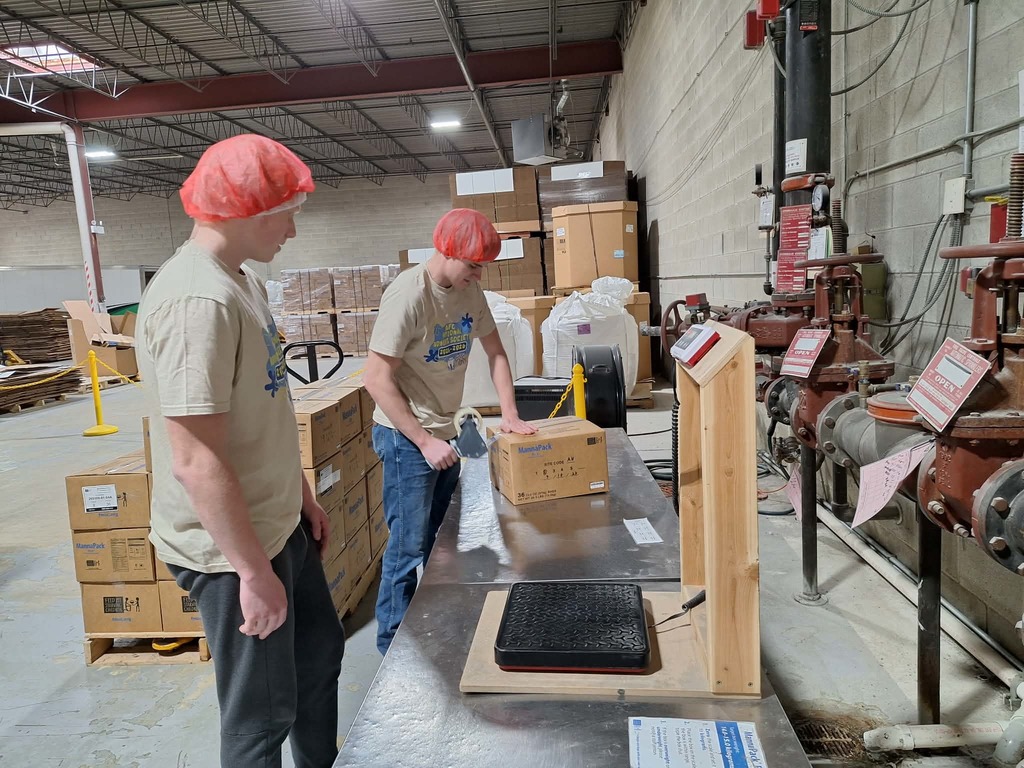 two students boxing up goods wearing hair nets and working hard