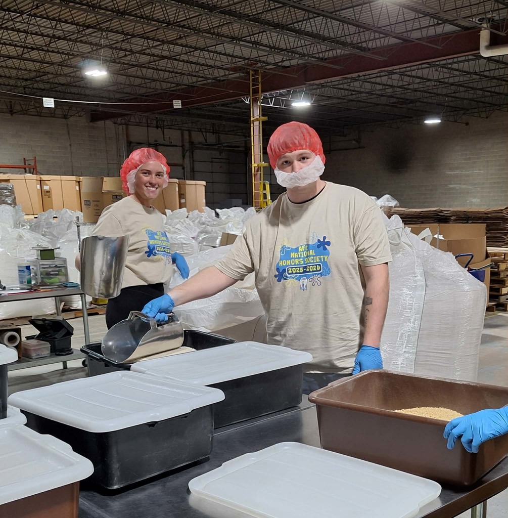 two male students in haor nets, gloves smiling for camera as scooping up food to box. 