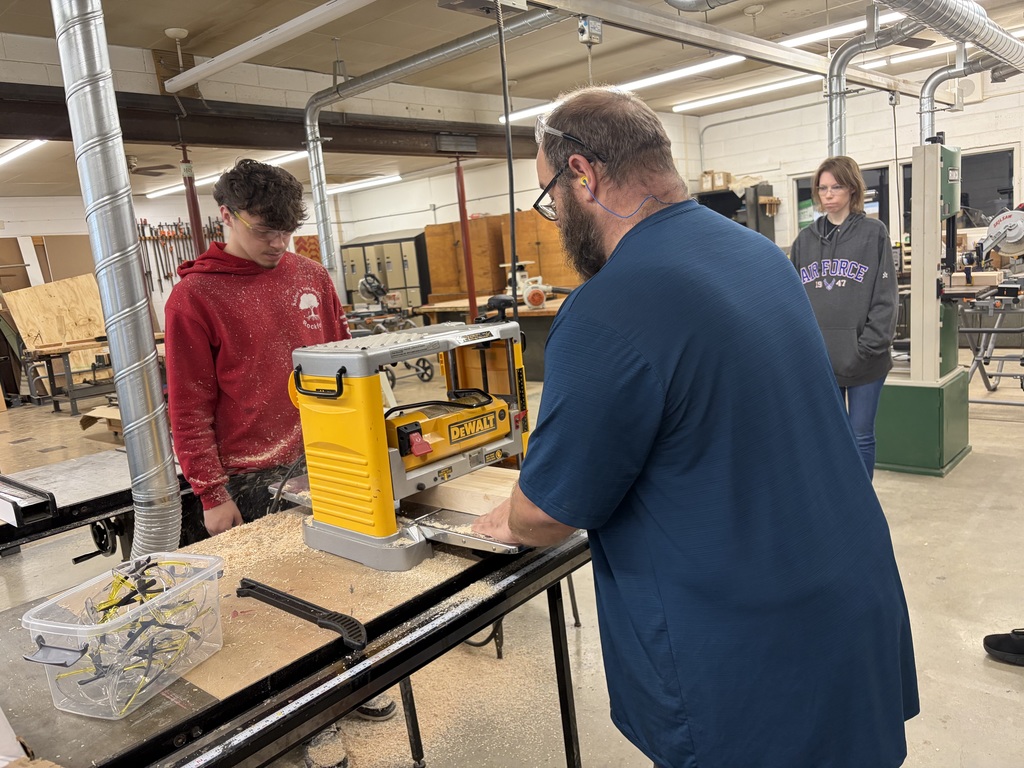teacher showing high school student how to use a saw wood.