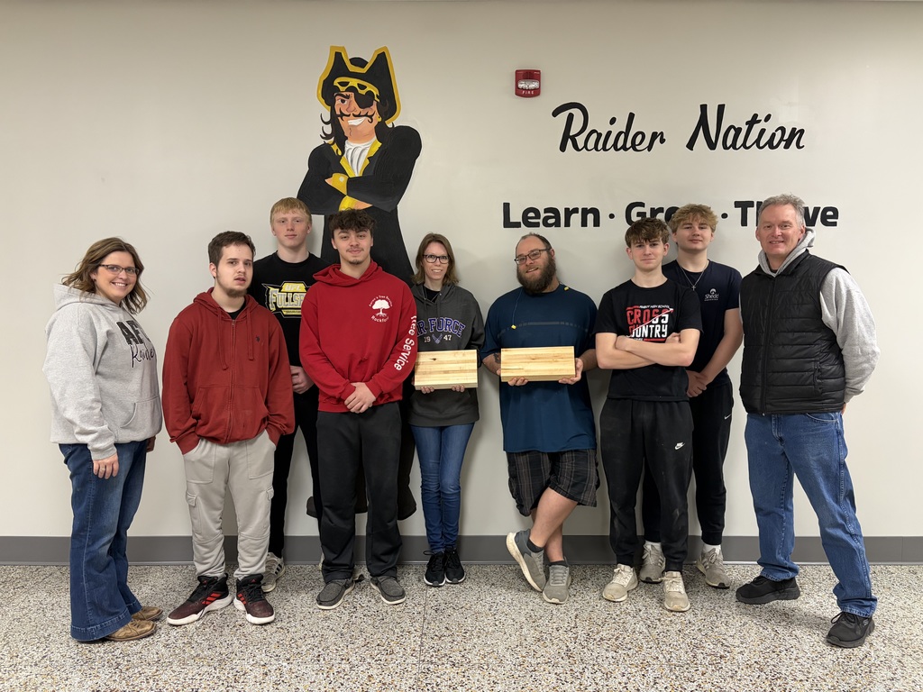 students posing in front of raider nation wall