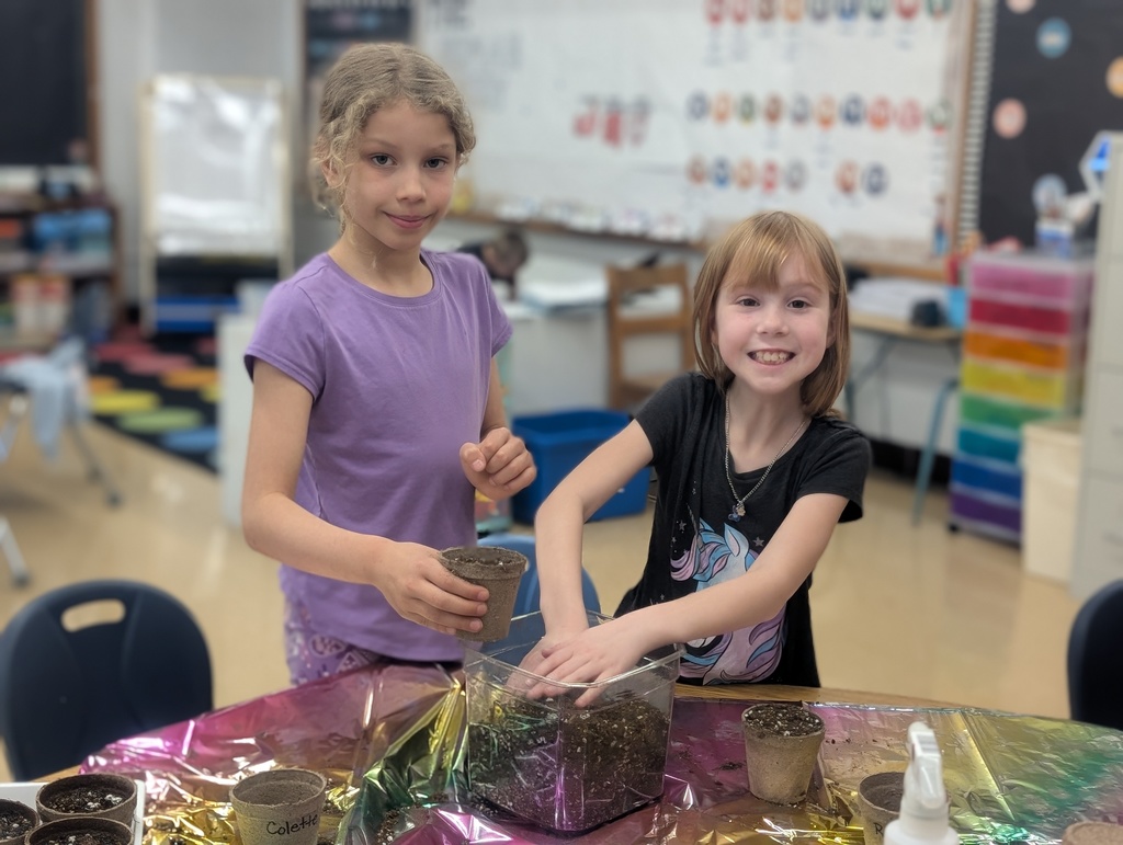 two female students smiling at the camera packing dirt