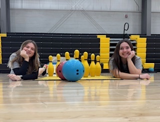 two female students laying on ground by bowling balls and pins