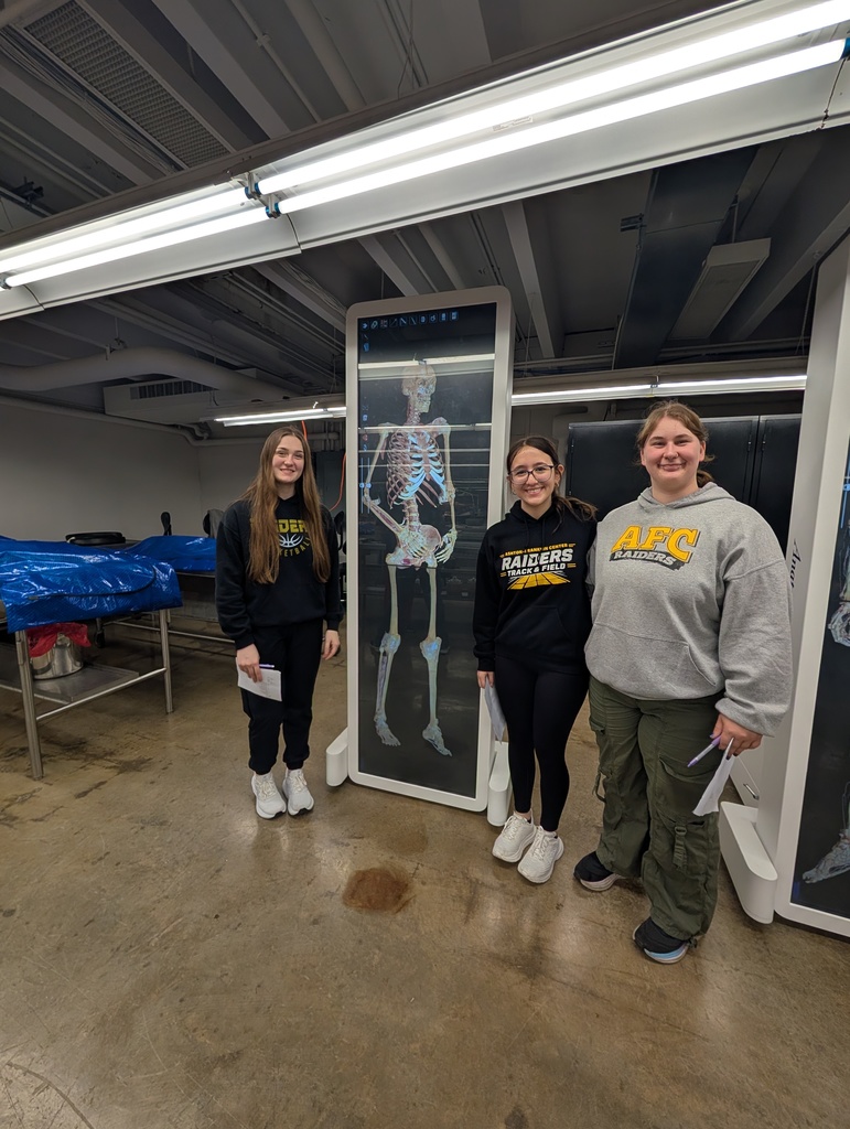 Three female students posing in front of wall of a skeleton at the university 