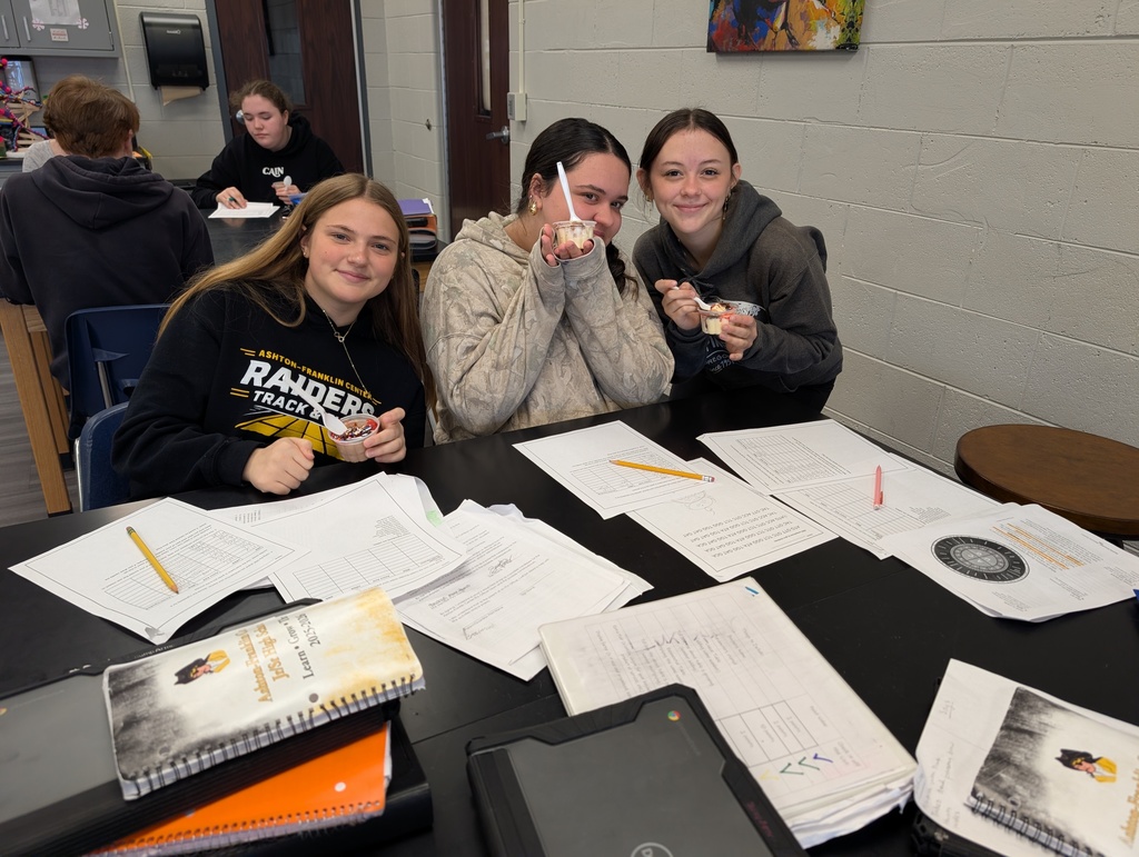 three female students smiling with ice cream in their hands sitting at the science table