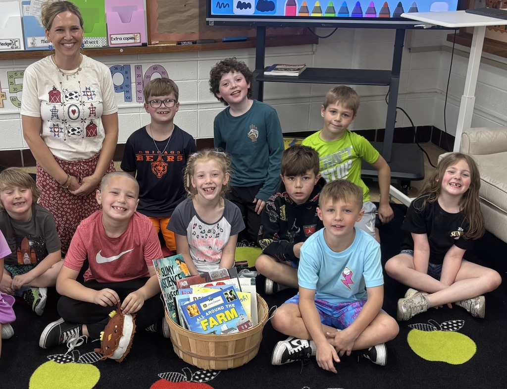 Mrs. Wolf and the class sitting on the carpet with a bin of the donated books - students are smiling