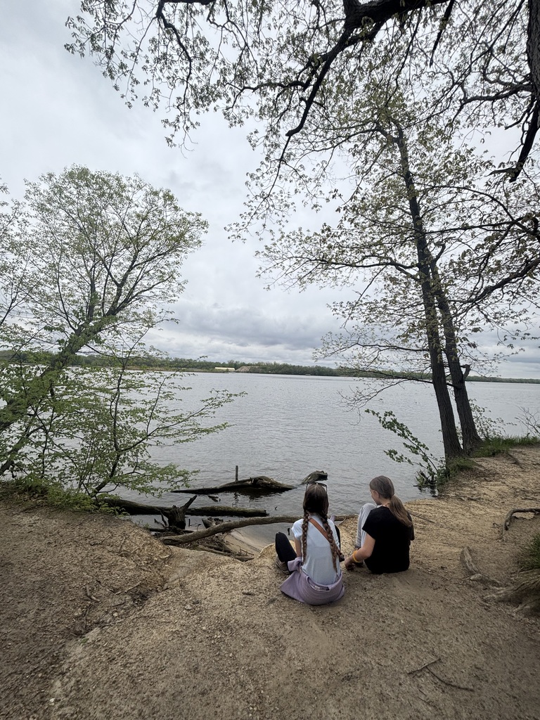 two girls sitting on the ground looking toward the water