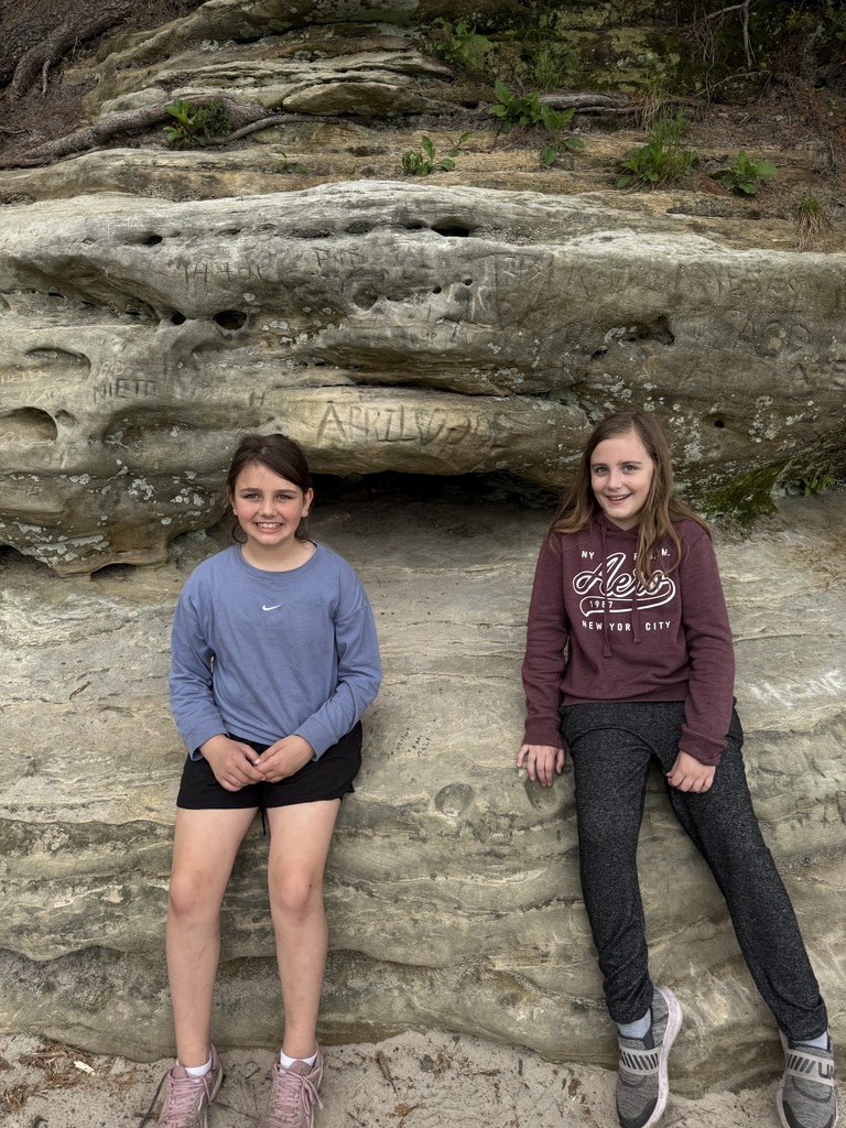 two girls sitting on a rock posing