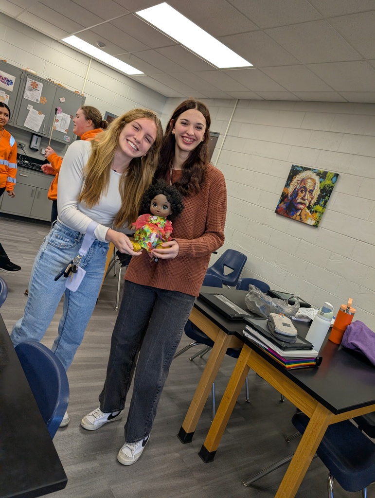 two female students smiling holding a doll