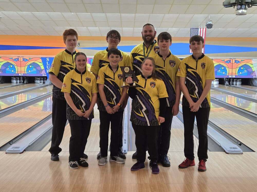 Six Affton High School bowling club members in matching yellow and black jerseys smiling together on a bowling lane with their coach and a trophy.