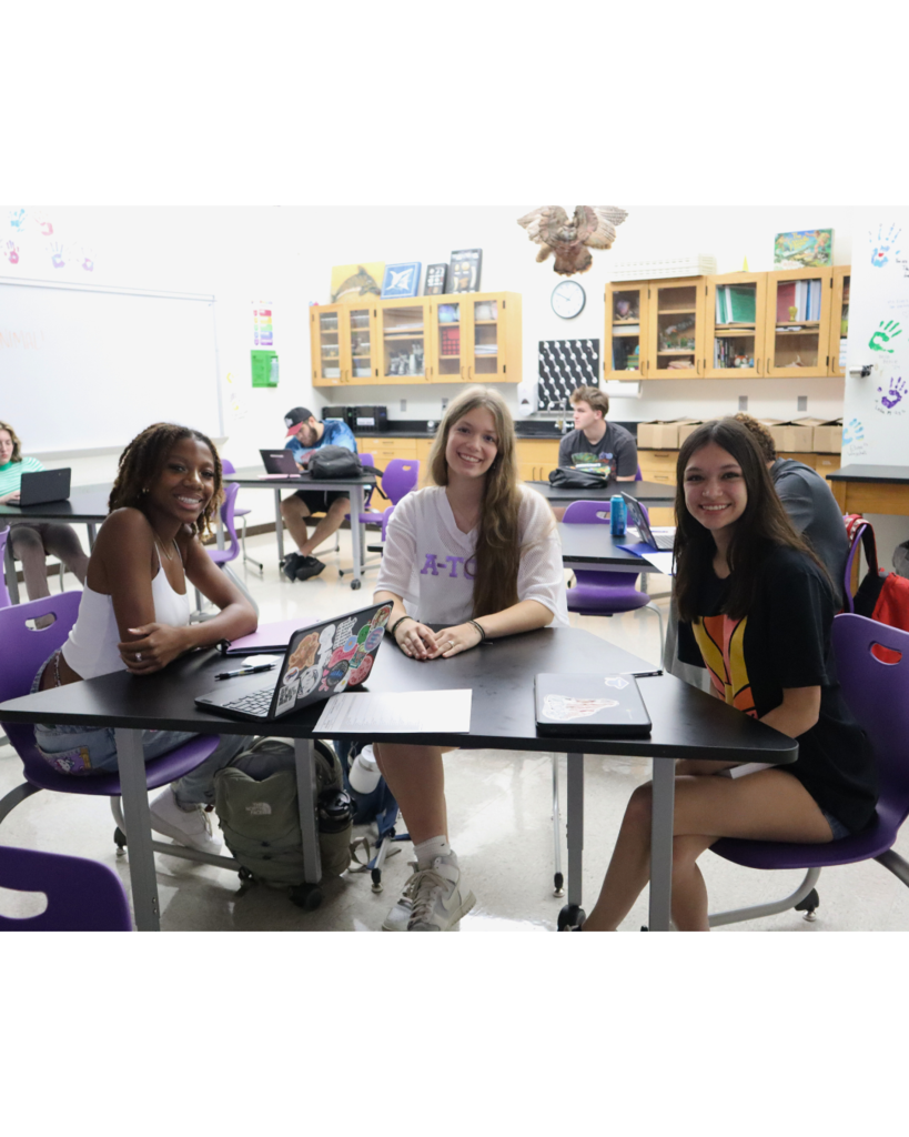 Three high school girls are sitting in a classroom while looking at the camera and smiling