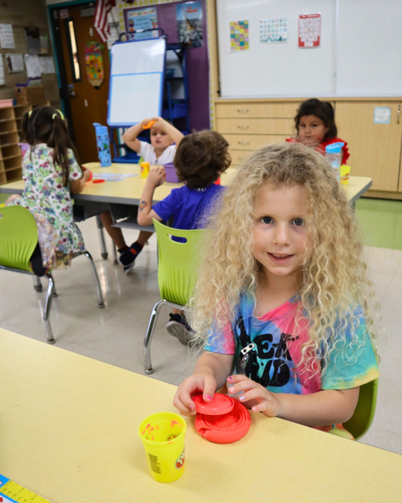 A kindergarten student with long blonde curls plays with Play-Doh