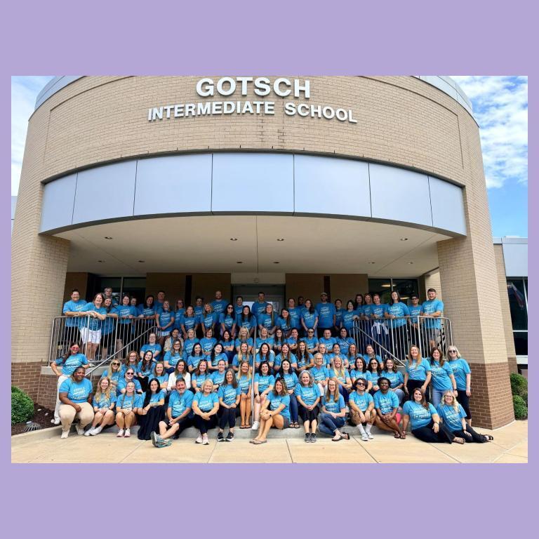 Gotsch staff sit on the front stairs of the school. They are all wearing matching shirts.