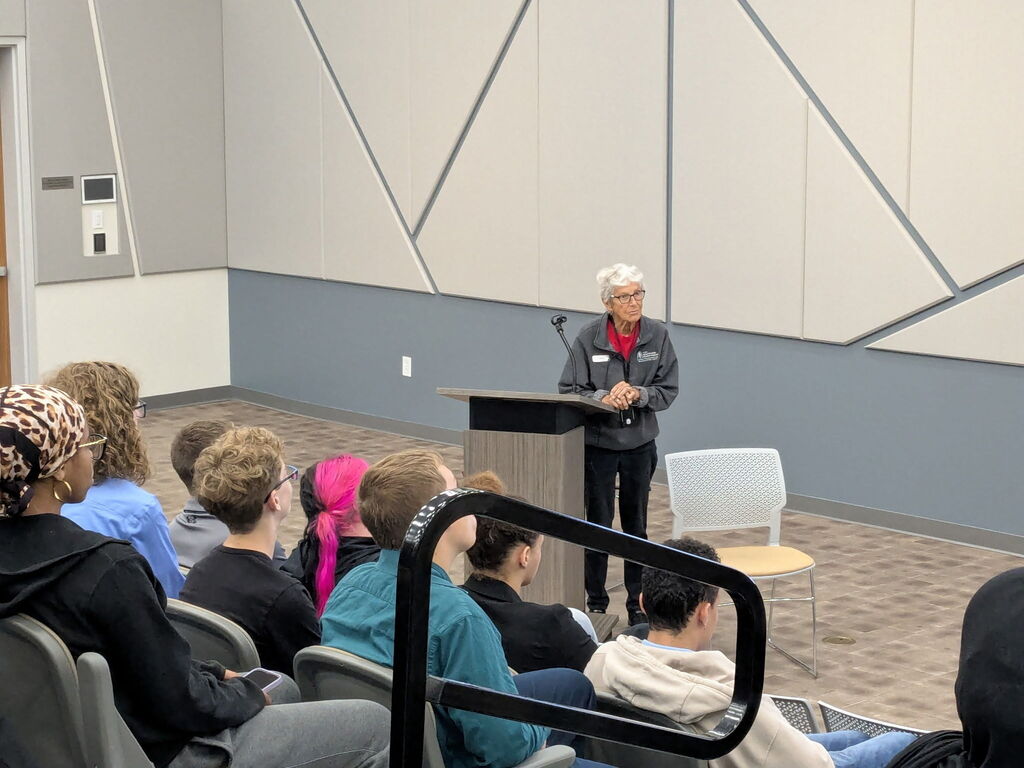 A speaker at a podium addresses a group of students seated in a modern auditorium