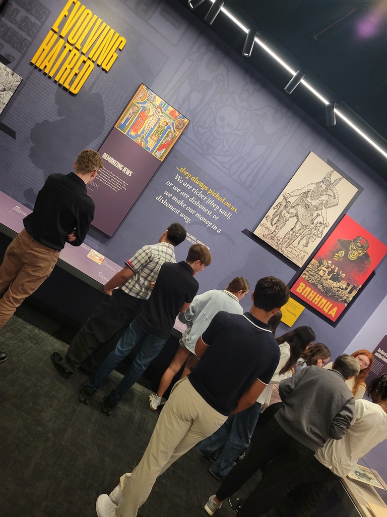 Students view informative wall panels titled 'Evolving Hatred' in an museum exhibit.