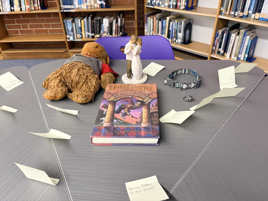 "A Harry Potter book on a table with a plush dog, a couple figurine, a collar, and fanned sticky notes in a library.