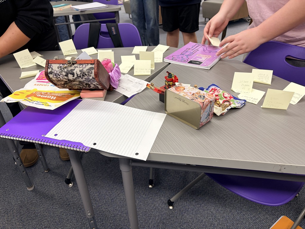 Hands collaborate, placing sticky notes on a grey table covered in notes and objects.
