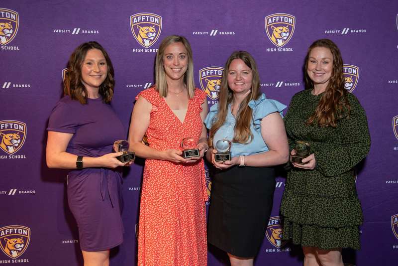 Four award-winning teachers stand together holding apple trophies in front of an Affton High School backdrop.