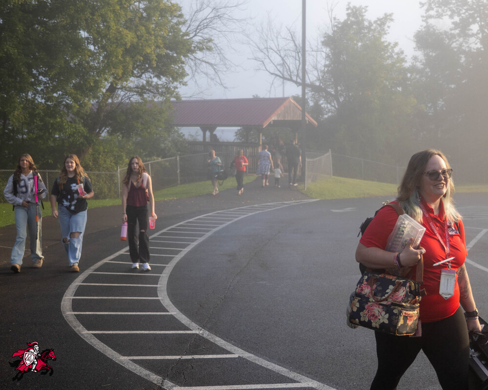 Students walk over a bridge and down a sidewalk in the direction of a school building
