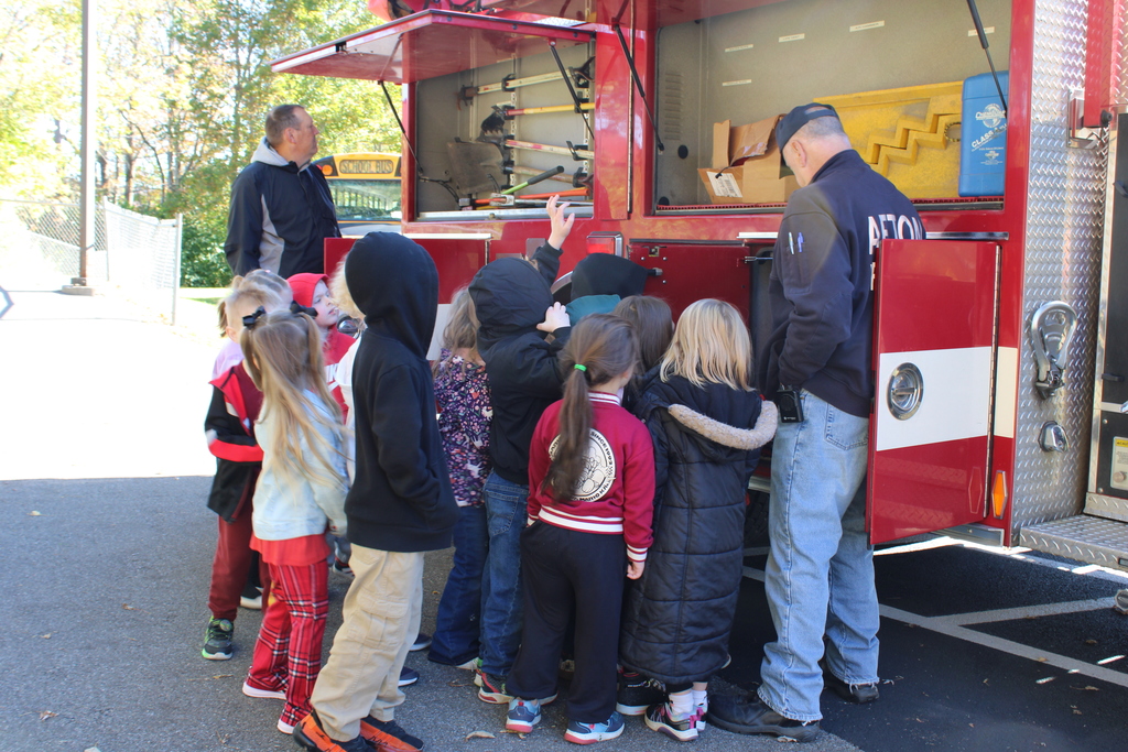 Fire fighter showing kids what is in the fire truck. Tools are visible from the tool compartment above.