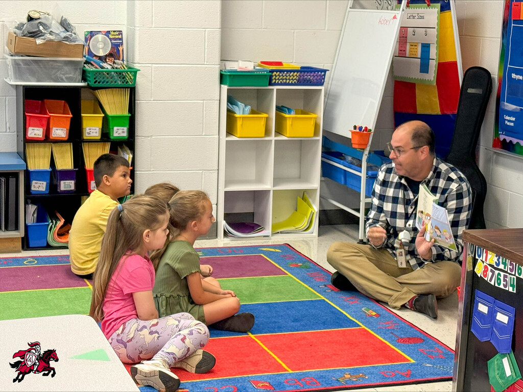 A teacher reads a book to pre-K and kindergarten students on the floor of a classroom