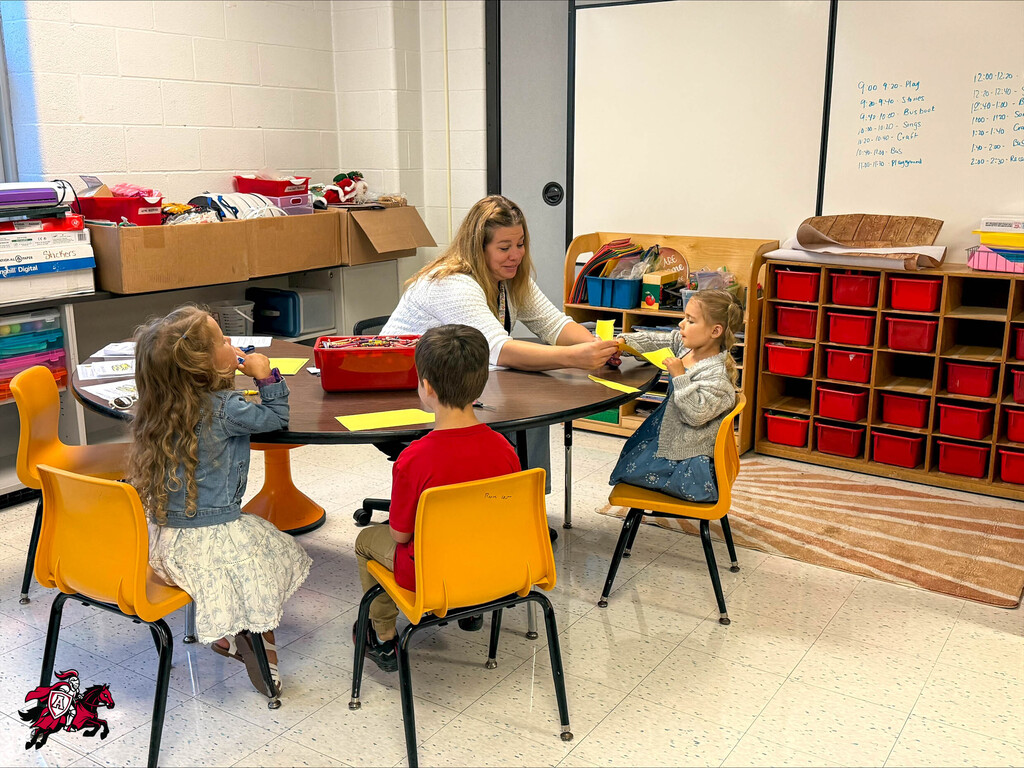 Pre-K and kindergarten students color with crayons on coloring pages at a table