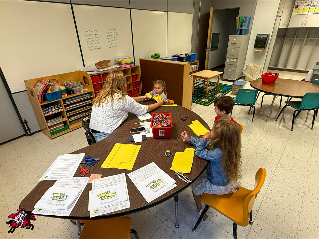 Pre-K and kindergarten students color with crayons on coloring pages at a table