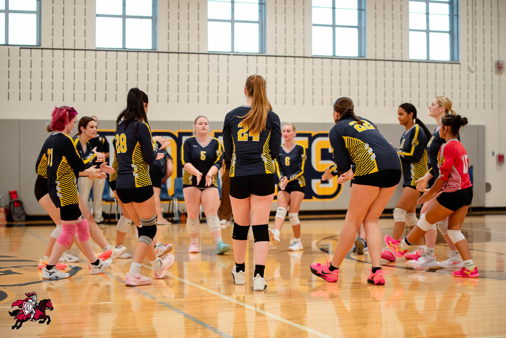 A team of female athletes in matching uniforms walks and converses on an indoor basketball court.