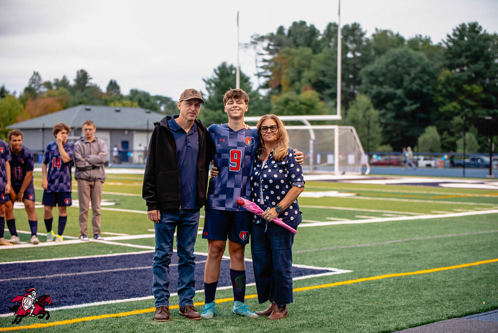 A family stands on a field, with one wearing a number 9 jersey. They pose with a young man.