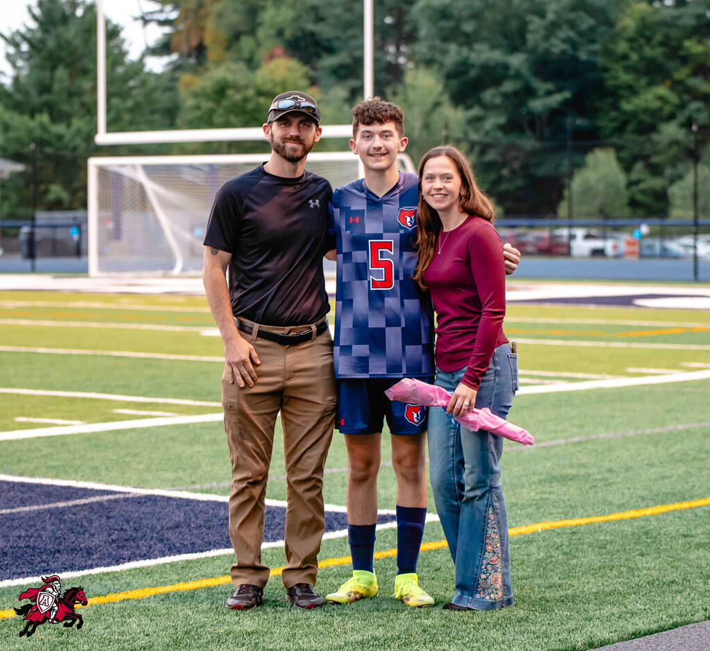 Three people on a football field. One wears a blue and white jersey with number 5.