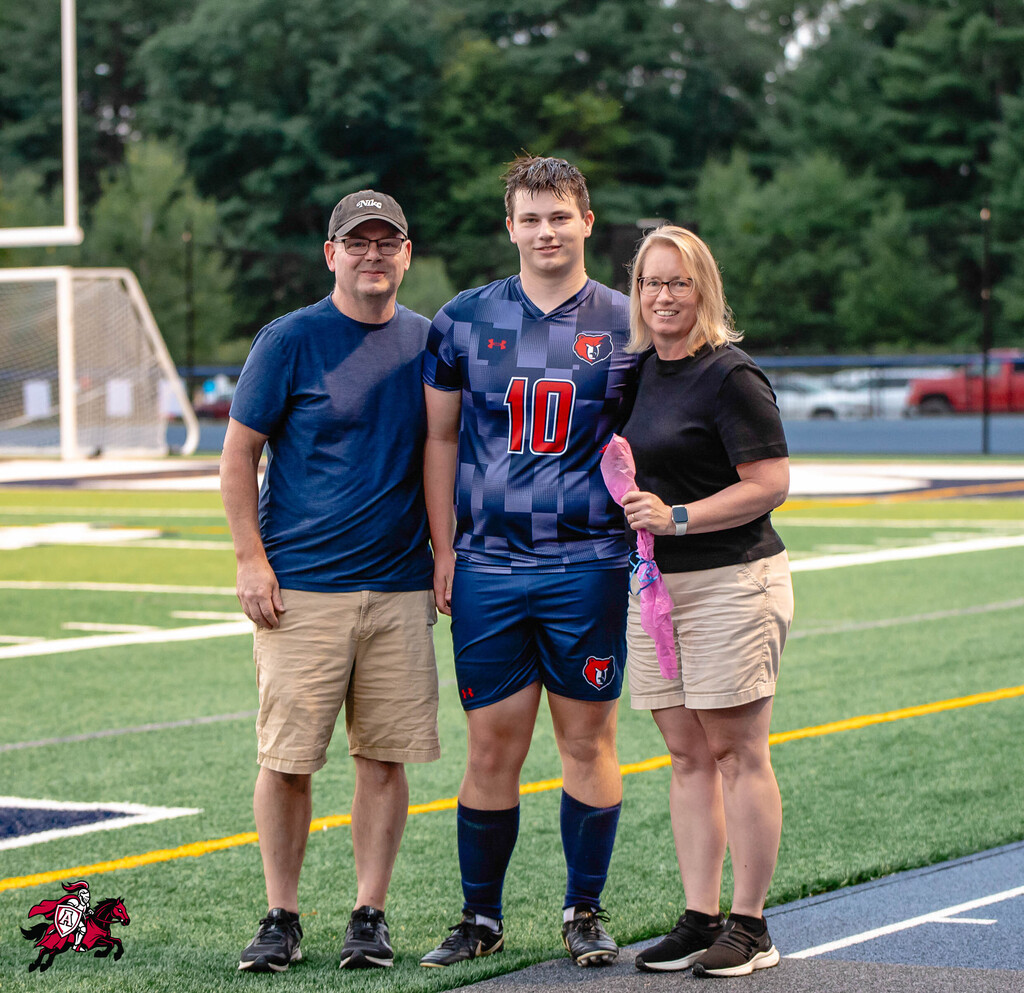 Three individuals on a field, one wearing a blue jersey with the number 10, another in a cap and blue shirt, and the third in a black shirt.