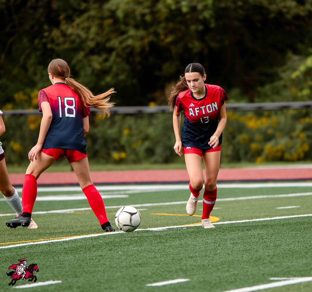 Two female soccer players on a field, one with the number 18, the other with "AFTON" on their jerseys.