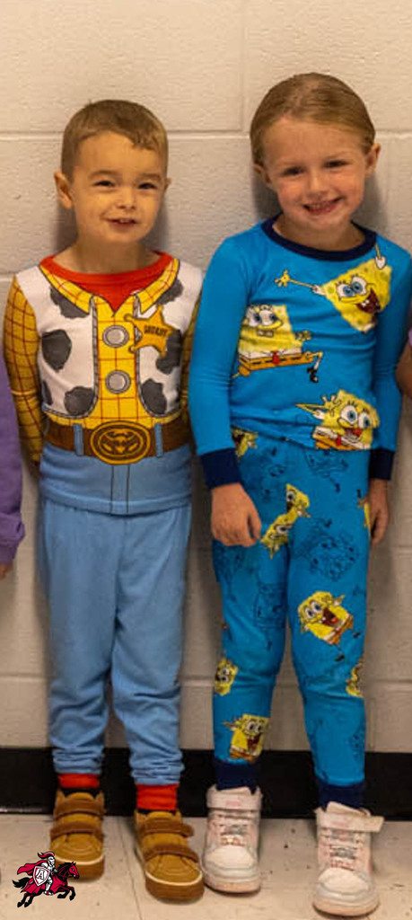 Two children, one in cowboy pajamas and the other in Spongebob pajamas, stand side by side. They are against a white wall.