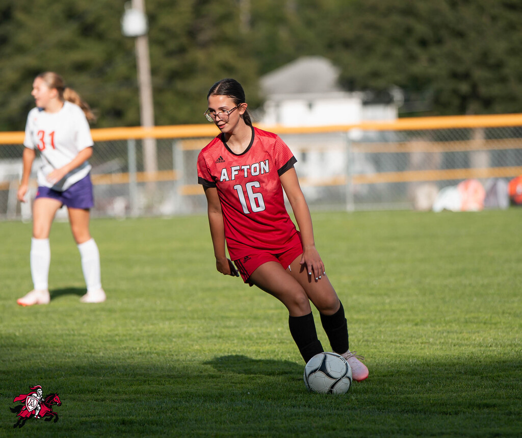 Two players on a soccer field, one in a red jersey, number 16, preparing to kick a ball.