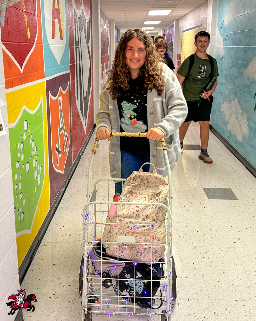 A woman with curly hair pushes a small shopping cart with bags down a colorfully decorated hallway.