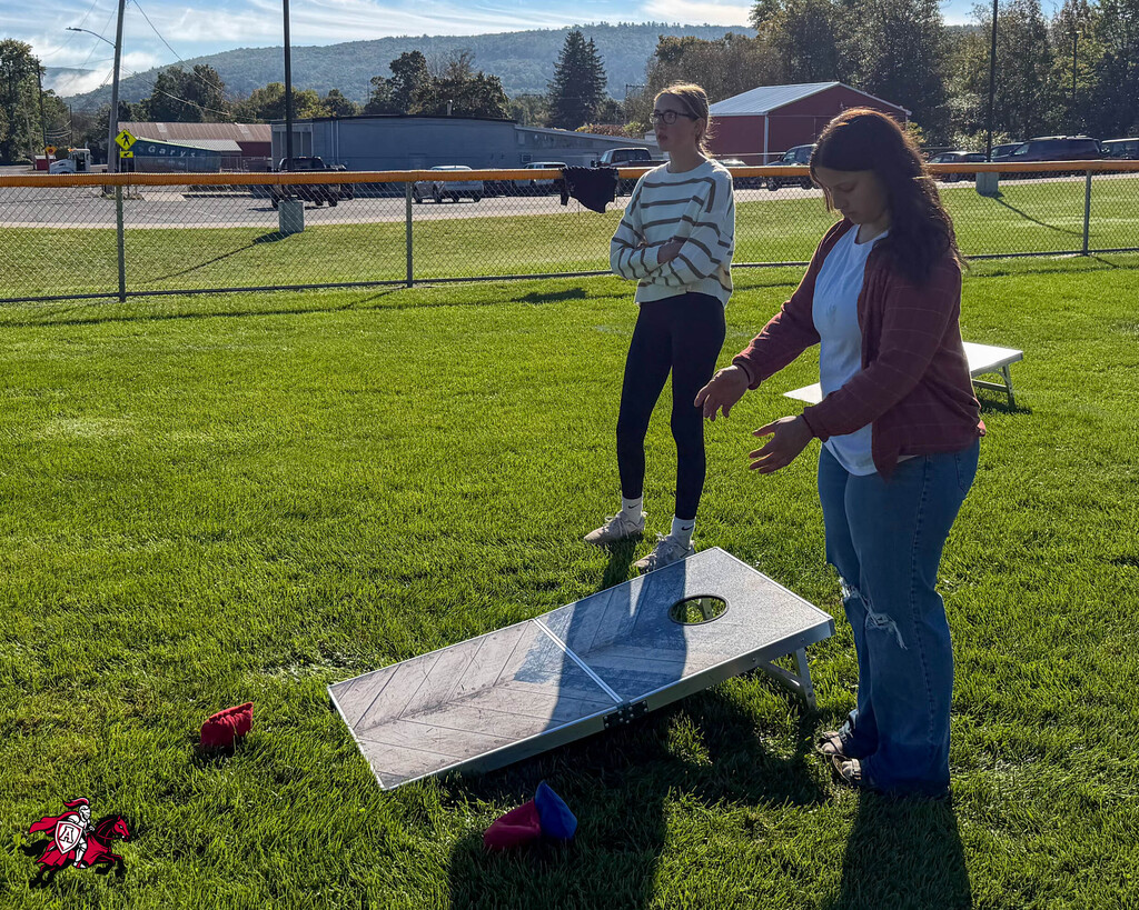 Two people on a grass field with a cornhole game set up in front of them.
