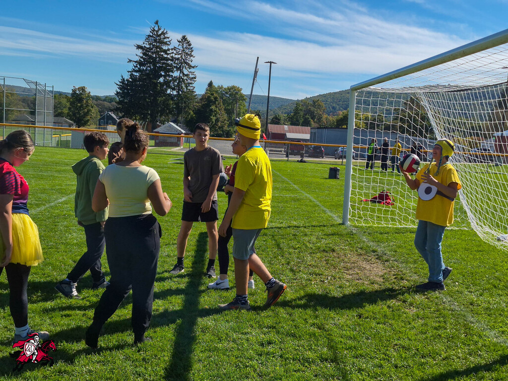 Group of people in casual clothes on a grassy field, with a soccer goal in the background.