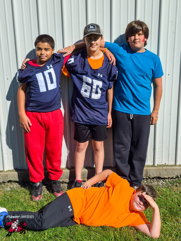 Four children in sportswear. One wearing blue, another orange, one in blue with a white number 10, and the last in blue.