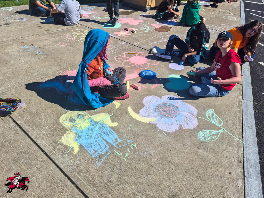 Multiple people are seated on concrete with colorful chalk drawings, including flowers, behind them.